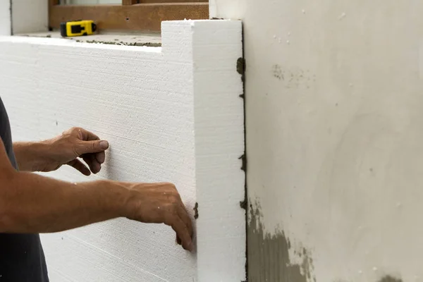Worker hands installing white rigid polyurethane foam sheet on plastered brick wall. Modern technology, renovation, insulation concept.