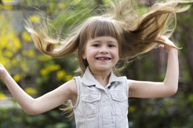 Güzel bir uzun saçlı sarışın okul öncesi kız utanarak kamera karşısına içine gülümseyerek kolsuz beyaz elbiseli portresi açık havada arka plan bulanık. Masum mutlu çocukluk kavramı.