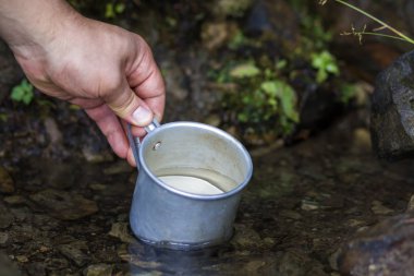 Adam el temiz tatlı su içmek için doğal dağ dere üzerinden scooping turistik alüminyum Kupası ile yakın çekim. Turizm, aktif yaşam tarzı, Doğa ve kirliliği sorunları kavramı.