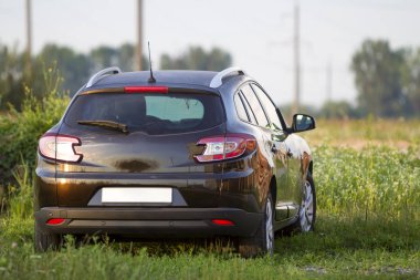 Modern yeni parlak boş siyah araba arkadan görünüm yol çimenli başgösteren alanındaki parlak yaz güneşli bulanık yeşil ağaçlar arka plan üzerinde dışarıda. Ulaştırma, kirlilik ve ekoloji kavramı.