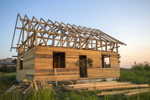 New cottage of natural ecological lumber materials under construction in green field. Wooden walls and steep roof frame. Property, investment, professional building and reconstruction concept.