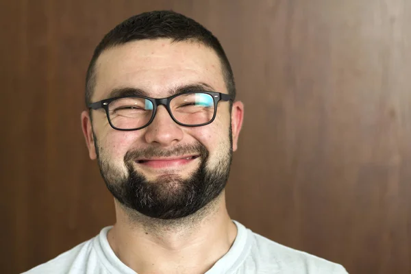 Portrait of handsome bearded black haired intelligent modern young man in glasses with short haircut and kind black eyes smiling on blurred background. Youth and confidence concept.