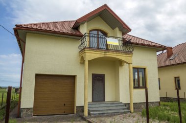 Yeni sarı iki katlı konut yazlık shingle çatı, ön sundurma, plastik pencere, yüksek bacalar, mavi gökyüzü arka plan üzerinde balkon ile. Gayrimenkul mülkiyet, mimari ve refah kavramı.