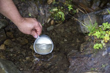 Adam el temiz tatlı su içmek için doğal dağ dere üzerinden scooping turistik alüminyum Kupası ile yakın çekim. Turizm, aktif yaşam tarzı, Doğa ve kirliliği sorunları kavramı.