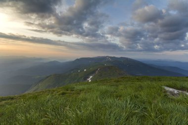 Geniş Yataklı güneş doğarken yaz. Parlayan turuncu güneş mavi bulutlu gökyüzü yeşil çimenli tepe yumuşak çim ve uzak dağ üzerinde yükselterek sabah sis ile kaplı. Doğa kavramının güzellik.