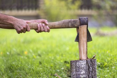 Güçlü kas adam yakın çekim el yakacak odun yığını ile eski keskin demir balta ile bulanık yeşil çimenli güneşli çiçeklenme üzerinde açık havada ağaç gövdesi kesim yaz çayır bokeh arka plan.
