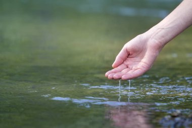 Güzel beyaz kadın el şefkatle dokunmadan Close-up, temiz tatlı su üzerinde scooping yeşil boşluk arka plan bulanık. Turizm, aktif yaşam tarzı, Doğa ve kirliliği sorunları kavramı.