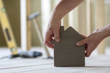 Kaslı erkek Close-up holding küçük kahverengi ahşap model ev araçları binanın arka plan bulanık eller. İnşaat, gayrimenkul ve rüya ev concept sahipliğini yatırımları.