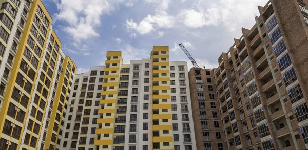 High rising multistory residential apartment brick building and working crane on block under construction on blue sky background. Modern urbane architecture, investments, buying and selling concept.