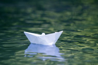 Basit küçük beyaz origami kağıt tekne sessizce parlak yaz göğün altında açık mavi nehir veya deniz suyu yüzen Close-up. Özgürlük, düşler ve fantasies kavramı, boşaltmak arka plan.