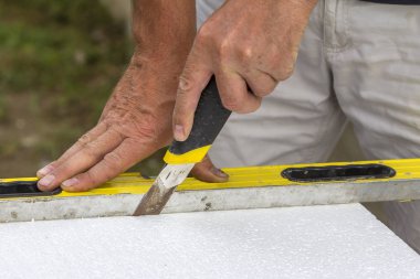 İşçi el bıçak ve ev yalıtım düzey kesme beyaz sert poliüretan köpük sayfasını Close-up. Modern teknoloji, yenileme, profesyonel iş, mineral yün kavramı için alternatif.