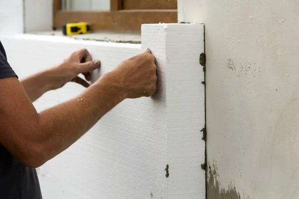 Worker hands installing white rigid polyurethane foam sheet on plastered brick wall. Modern technology, renovation, insulation concept.