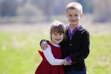 Güzel sarışın çocuk komik çocuk diş birlikte ayakta akıllı giysiler ile gülümseyen portresi üzerinde arka plan bulanık, kardeşi kucaklayan ablası açık. Mutlu dikkatsiz çocukluk kavramı.