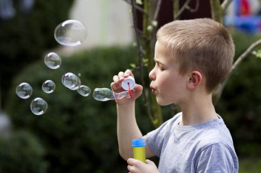 Profil sevimli yakışıklı küçük sarışın çocuk çocuk komik ciddi ifade üzerinde açık havada renkli şeffaf sabun köpüğü üfleme ile yeşil yaz arka plan bulanık. Sevinç dikkatsiz çocukluk kavramının.