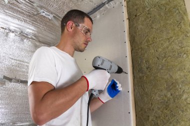 Gözlük yalıtımı çalışma tornavida ile işçi. Alçıpan Duvar kirişler, taş yünü personel ahşap çerçeve içinde yalıtım üzerinde. Rahat sıcak ev, ekonomi, inşaat ve tadilat kavramı.