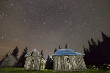 Eski ahşap yıpranmış boyanmamış çoban kulübe Karpat Dağları üzerinde çimenli çam ağaçları arasında güzel bir gece yaz yıldızlı gökyüzü altında karanlık siluetleri takas yeşil. Geniş açı, kopya alan arka plan.