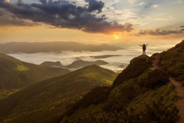 Geniş dağ panorama. Turist ile sırt çantası ile beyaz bulutlar kaplı vadi üzerinden kaldırdı elleriyle kayalık dağ yamacında küçük silüeti. Güzellik, Doğa, turizm ve seyahat kavramı