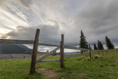 Yeşil çimenli Vadisi yamaç ilkel ahşap çit ve kapı ile panoramik yaz görünümünü gündoğumu, mavi bulutlu gökyüzü altında uzak odunsu sisli dağda. Güzellik, Doğa ve kavram seyahat.