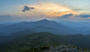 Fantastik gündoğumu veya günbatımı üzerinde yeşil dağ sırtı ile yoğun mavi sis kaplı. Parlak turuncu güneşin yumuşak bulutlu gökyüzü uzak ufukta yükselterek. Güzellik, Doğa, turizm ve seyahat kavramı.