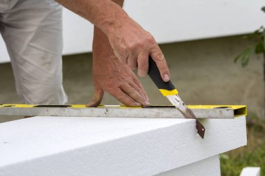 İşçi el bıçak ve ev yalıtım düzey kesme beyaz sert poliüretan köpük sayfasını Close-up. Modern teknoloji, yenileme, profesyonel iş, mineral yün kavramı için alternatif.