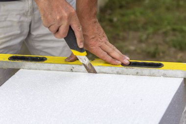 İşçi el bıçak ve ev yalıtım düzey kesme beyaz sert poliüretan köpük sayfasını Close-up. Modern teknoloji, yenileme, profesyonel iş, mineral yün kavramı için alternatif.