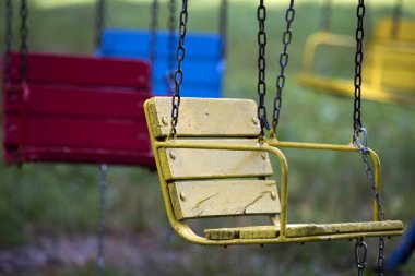 Yakın çekim boş ahşap boyalı mavi, sarı, antika koltuk sandalye çok renkli atlıkarınca açık yeşil güneşli günü şehir eğlence parkında açık ile zincir asılı olan arka plan bulanık..