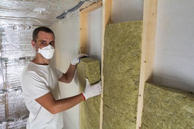 Taşyünü yalıtım personel için soğuk bariyer için gelecekteki ev duvarları ahşap çerçeve içinde yalıtım solunum genç işçi. Rahat sıcak ev, ekonomi, inşaat ve tadilat kavramı.