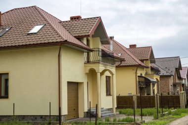 Yeni sarı iki katlı konut yazlık shingle çatı, ön sundurma, plastik pencere, yüksek bacalar, mavi gökyüzü arka plan üzerinde balkon ile. Gayrimenkul mülkiyet, mimari ve refah kavramı.