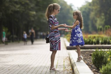 Genç sarışın uzun saçlı çekici kadın ve kız küçük çocuk güneş gözlüğü ve şık elbiseler güneşli park sokak üzerinde el ele tutuşarak profili tam uzunlukta portresi. Mutlu aile ilişkileri kavramı.