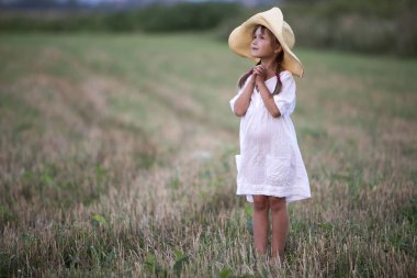 Full-length portrait of young fashionable lovely cute girl with long braids in nice white summer dress and big straw hat looking upwards on blurred grassy light green sunny field background. clipart