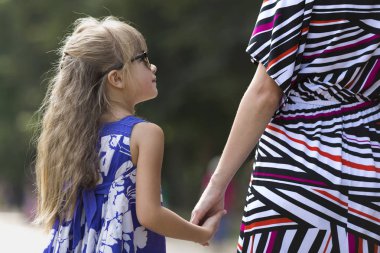 Arkadan görünüşü moda mavi elbise ve genç kadının elini açık havada bulanık renkli güneşli yaz bokeh arka planda tutarak güneş gözlüğü güzel uzun sarı saçlı kız çok genç çocuk.