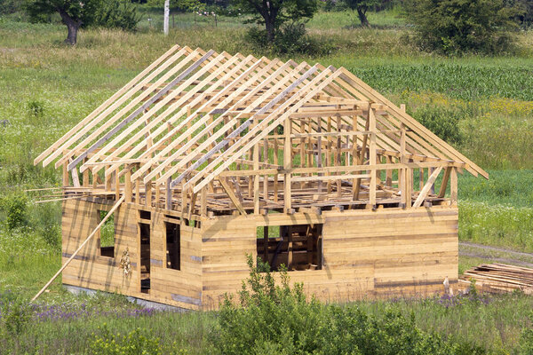 New wooden cottage of natural lumber materials with steep plank roof frame under construction in green neighborhood. Property, investment, professional building and reconstruction concept.