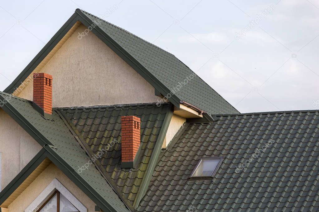 Close-up detail of new modern house top with shingled green roof, high brick-red chimneys and stucco walls. Professionally done building and construction work, real estate property, contract concept.