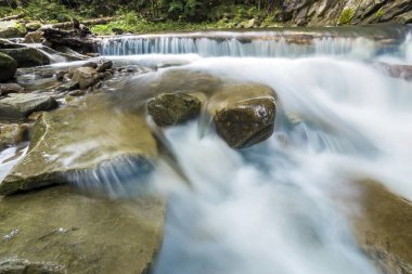 Küçük dağ vahşi yeşil orman Nehri ile büyük ıslak düşen kristal berraklığında yumuşak ipeksi su akan hızlı güzel şelaleler üzerinde parlak güneşli yaz günü taşlar. Uzun pozlama vurdu.