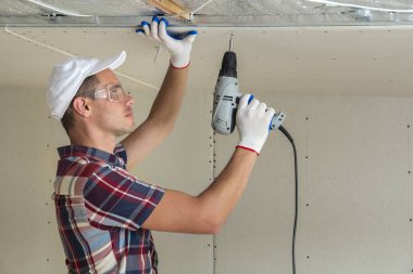 Alçıpan sabitleme Gözlük Genç adam metal çerçeve parlak alüminyum folyo ile yalıtımlı tavanda Elektrikli tornavida kullanarak tavana askıya. Tadilat, inşaat, do It yourself konsepti.