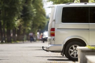 Yan görünümü ayrıntılı beyaz yolcu orta boy Lüks Minibüs Van yaz şehir sokak kaldırım bulanık siluetleri ile yaya yeşil ağaçlar bokeh kopya alan arka plan üzerinde Park.