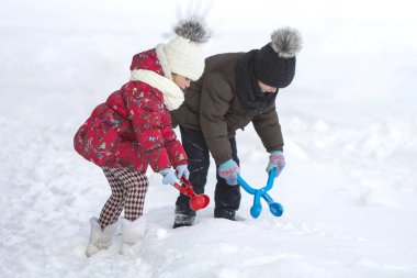 İki sevimli küçük çocuklar eğleniyor oynamak parlak kar kliplerle sıcak giysiler içinde kartopu beyaz kış soğuk günde parlak yapmak kopya alan arka plan bulanık. Açık havada etkinlik, tatil oyunları.