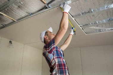Yakışıklı delikanlı casual giyim Alçıpan Asma Tavan tavan yalıtımlı alüminyum folyo ile üzerinde metal çerçeve bağlı ölçümü alır. İnşaat, tadilat, DIT kavramı.