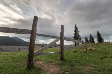 Yeşil çimenli Vadisi yamaç ilkel ahşap çit ve kapı ile panoramik yaz görünümünü gündoğumu, mavi bulutlu gökyüzü altında uzak odunsu sisli dağda. Güzellik, Doğa ve kavram seyahat.