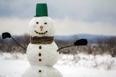 Turuncu havuç burun ile beyaz mutlu kardan adam portresi, siyah gözleri ve onun başında kış ortamda açık havada yeşil kova için Noel ve yeni yıl taşlar.