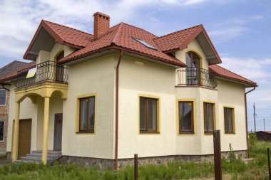 Yeni sarı iki katlı konut yazlık shingle çatı, ön sundurma, plastik pencere, yüksek bacalar, mavi gökyüzü arka plan üzerinde balkon ile. Gayrimenkul mülkiyet, mimari ve refah kavramı.