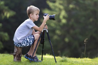 Ağaç kütüğü çimenli takas tripod fotoğraf makinesi ile çekim üzerinde oturan genç sarışın çocuk çocuk.