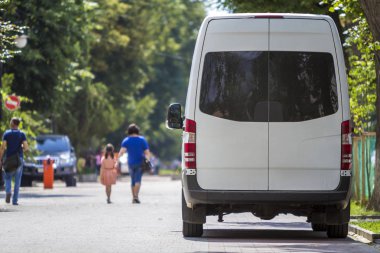 Geri görüntülemek beyaz yolcu orta boy ticari Lüks Minibüs Park van n gölgesi yeşil ağaç yaz şehir sokak ben yayalar ve otomobil yeşil ağaçların altında bulanık siluetleri ile.