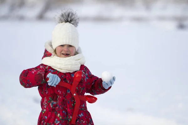 可爱的小年轻滑稽的无牙的女孩在温暖的衣服玩有乐趣做雪球在冬季寒冷的天白色明亮模糊复制空间背景 户外活动 假日游戏 — 图库照片
