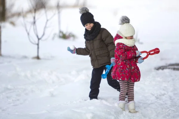 两个可爱的孩子在温暖的衣服与明亮的雪剪辑玩有乐趣做雪球在冬季冷天白色明亮模糊复制空间背景 户外活动 假日游戏 — 图库照片