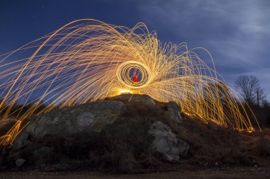 Uzun pozlama bir havai fişek duş parlak sarı parlak parıldıyor, mavi gece gökyüzü arka plan üzerinde yapım bir dairede çelik yün iplik, kayalık tepe üzerinde duran adam vurdu. Işık resim sanat kavramı.