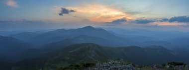 Fantastik gündoğumu veya günbatımı üzerinde yeşil dağ sırtı ile yoğun mavi sis kaplı. Parlak turuncu güneşin yumuşak bulutlu gökyüzü uzak ufukta yükselterek. Güzellik, Doğa, turizm ve seyahat kavramı.
