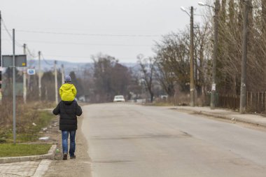 Arkadan görünüşü sıcak parlak giysiler serin bahar sisli sabahı banliyösü yol boyunca yürüyüş omuz genç çocuk taşıyan güçlü atletik adam baba. Ebeveyn-çocuk ilişkileri, sevgi ve bakım.