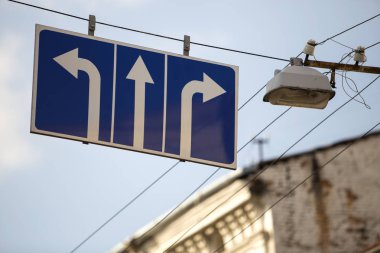 Yol işaret Close-up ulaşım hareket yönünde gösterilen mavi arka plan üzerinde üç beyaz oklarla Caddesi üzerinde yüksek lamba yakın tramvay hattına bağlı. Sipariş, seçim ve kuralları kavramı.