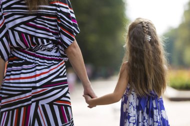 Oldukça küçük sarı uzun saçlı çocuk kız moda renkli elbise holding arka görmek trustingly el bulanık renkli güneşli yaz bokeh arka plan üzerine açık havada Genç kadın.